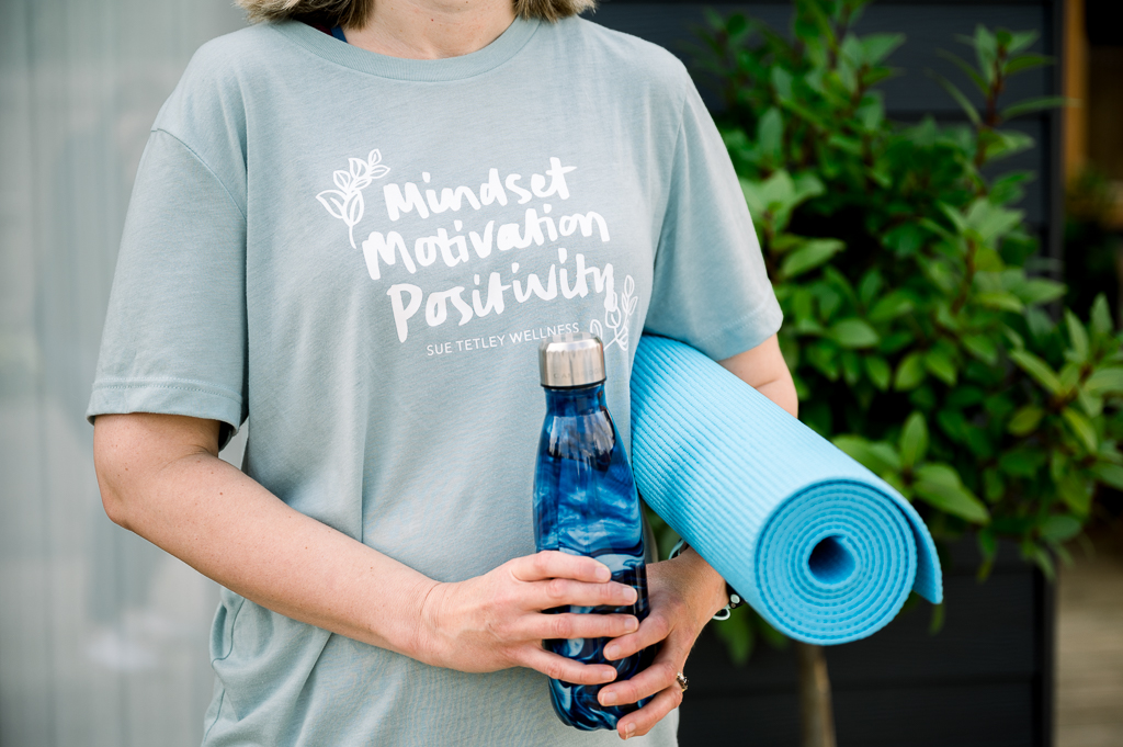 Woman holding a rolled yoga mat and water bottle with an inspirational t-shirt