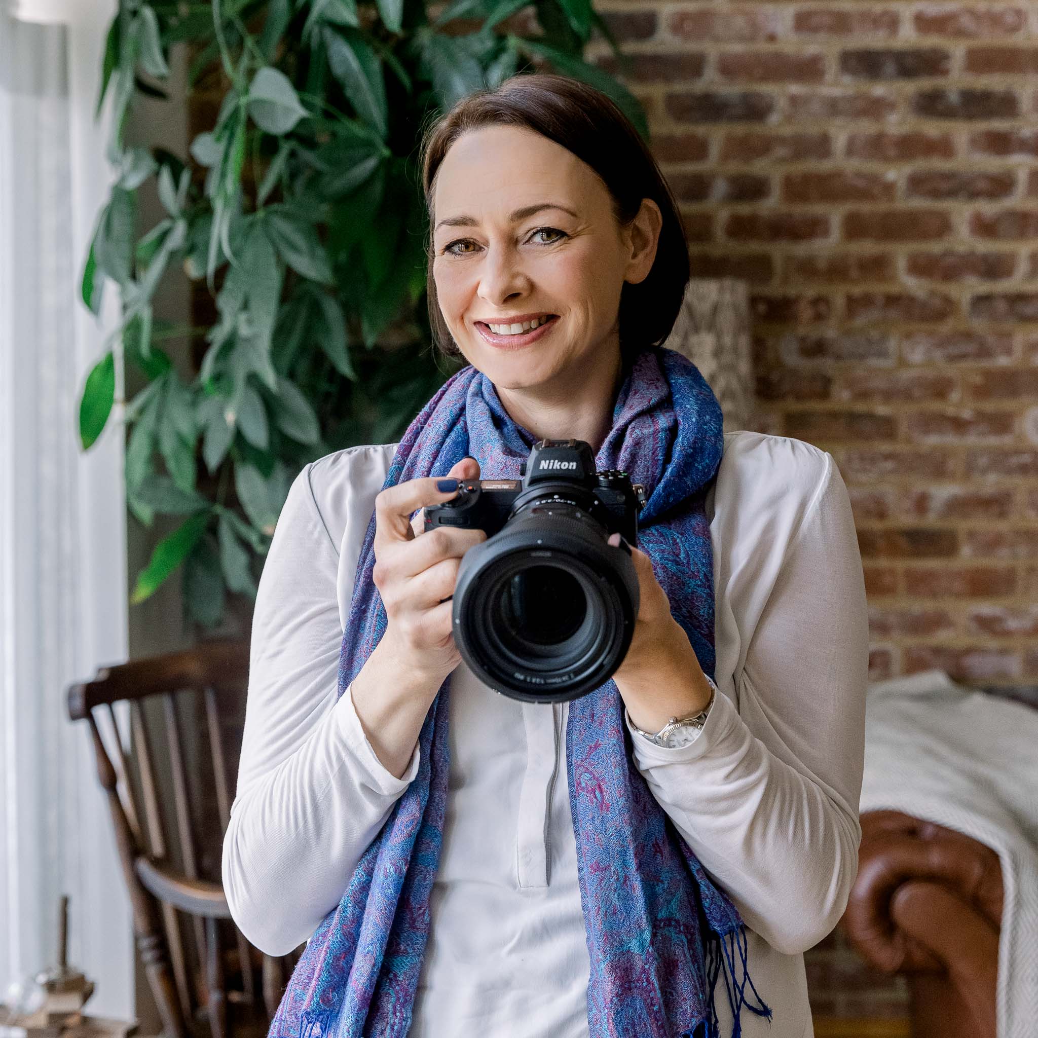 Picture of a brown haired woman holding a camera and smiling