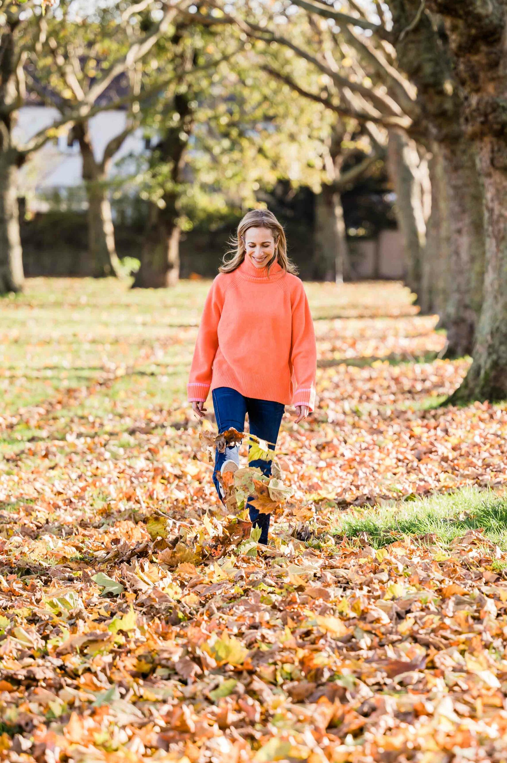 Smiling woman kicking through the autumn leaves in a London park