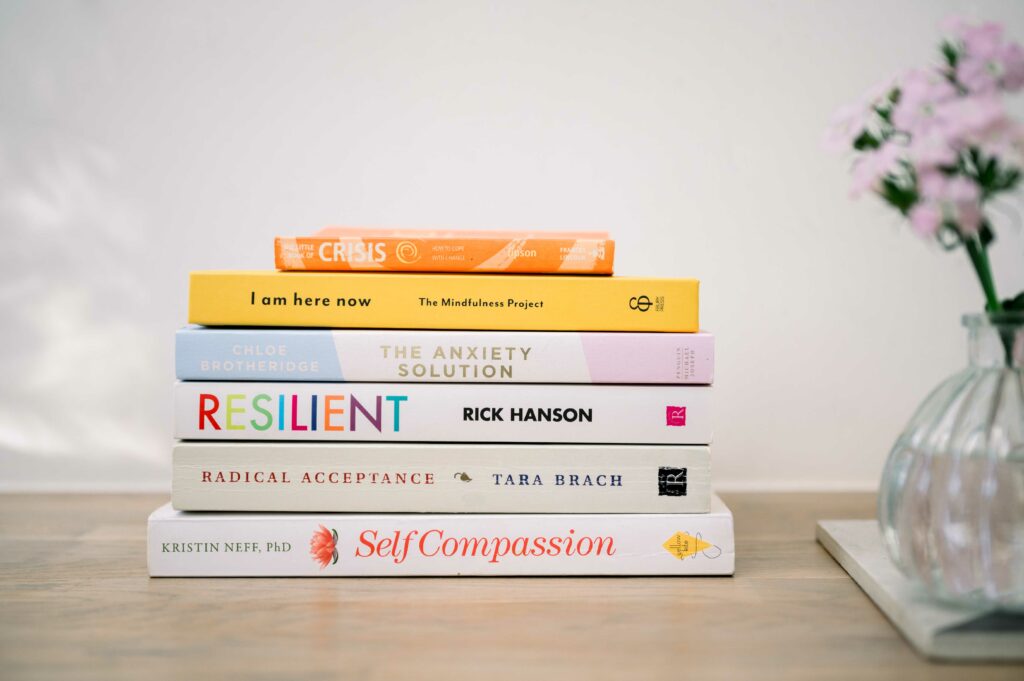 Pile of self awareness books on a wooden table with pink flowers to the right